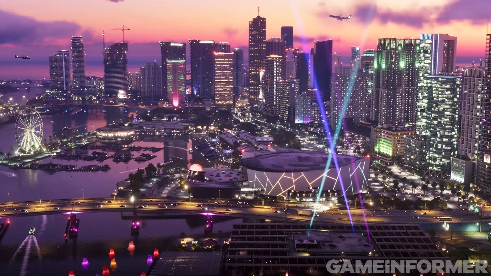 A skyline of towers lit up at night, with a Ferris wheel, a marina, a stadium and coloured searchlights pointing at the sky