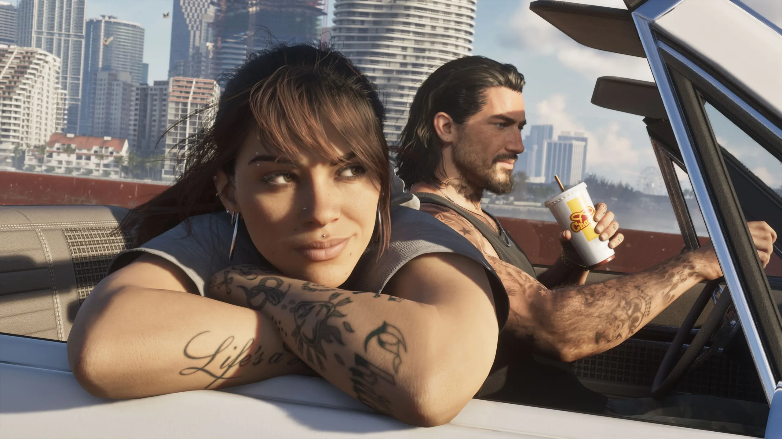 Lucia leaning on the door of a convertible Jason is driving, with city buildings behind them on a sunny day