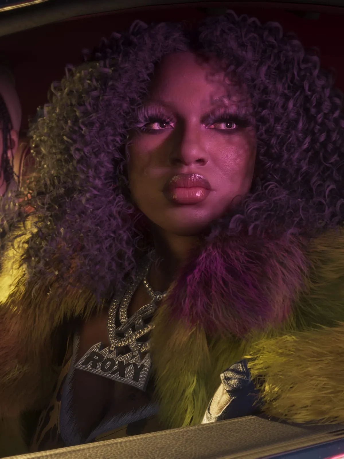 Roxy of the Real Dimez in a car seat, in a fur coat