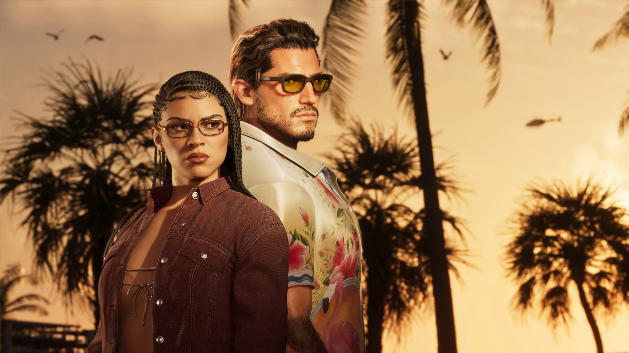 Jason, in sunglasses and a floral shirt, and Lucia, in glasses and a brown jacket, posing together among palm trees at sunset